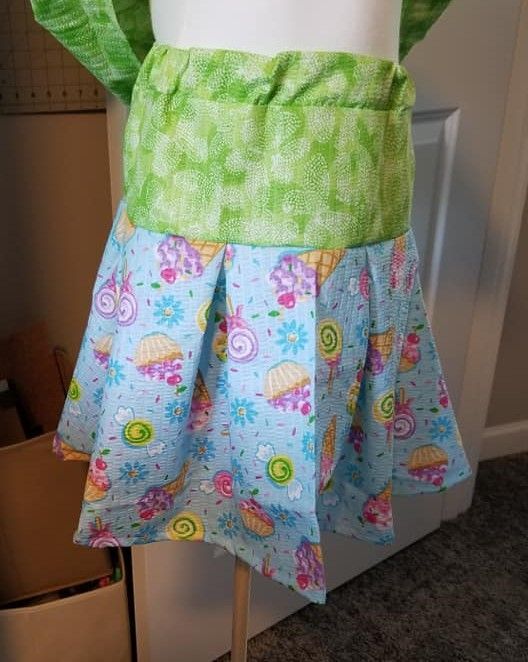 A handmade skirt on a mannequin, featuring a light blue fabric with a cupcake print and a green textured waistband.