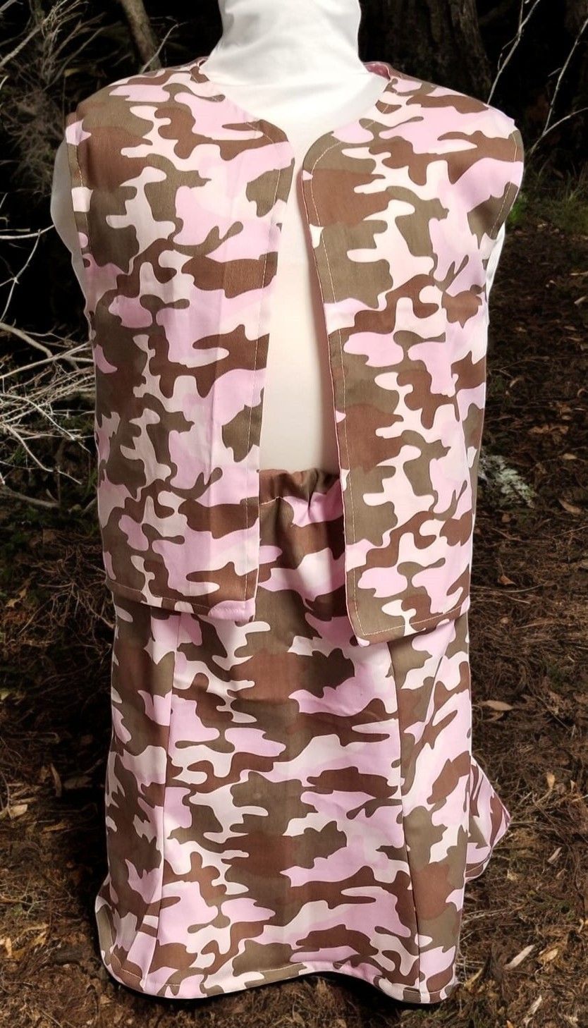 A pink and brown camouflage-patterned vest and matching skirt displayed on a mannequin against a wooded background.