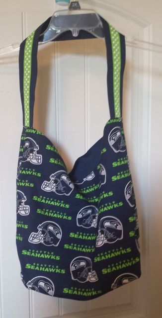 A handmade dark blue Seattle Seahawks fabric tote bag with a lime green geometric patterned strap, hanging on a hanger.