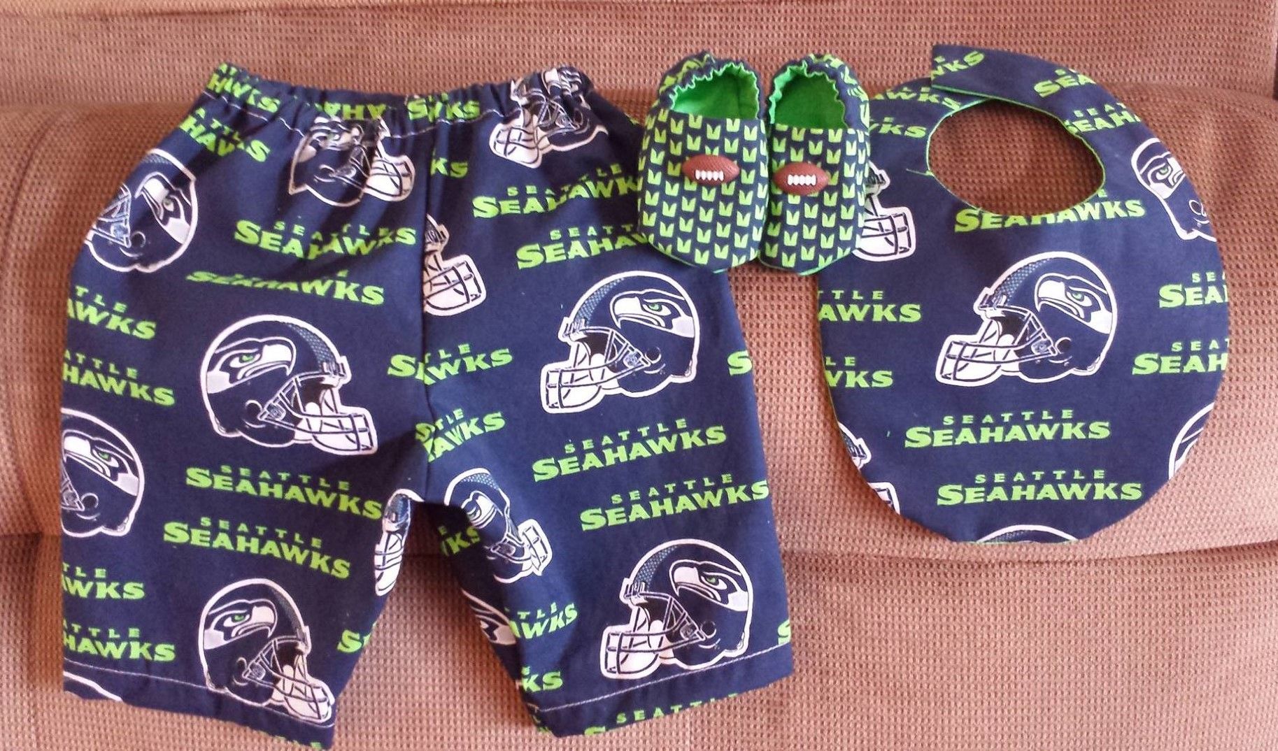 Seattle Seahawks themed baby set consisting of patterned navy blue pants, matching bib, and green accented booties.