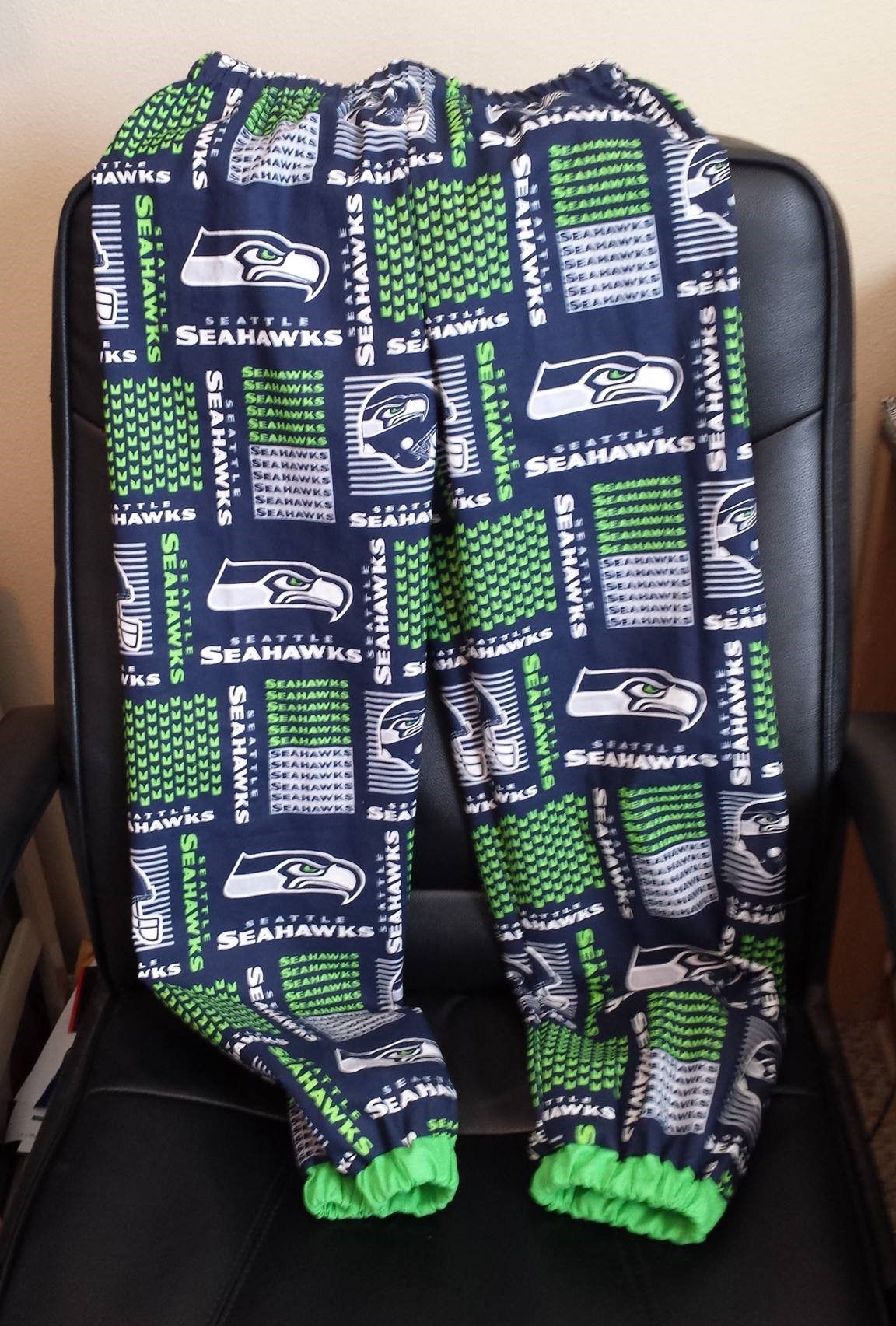 Seattle Seahawks patterned sweatpants with blue and neon green accents, resting on a black office chair.