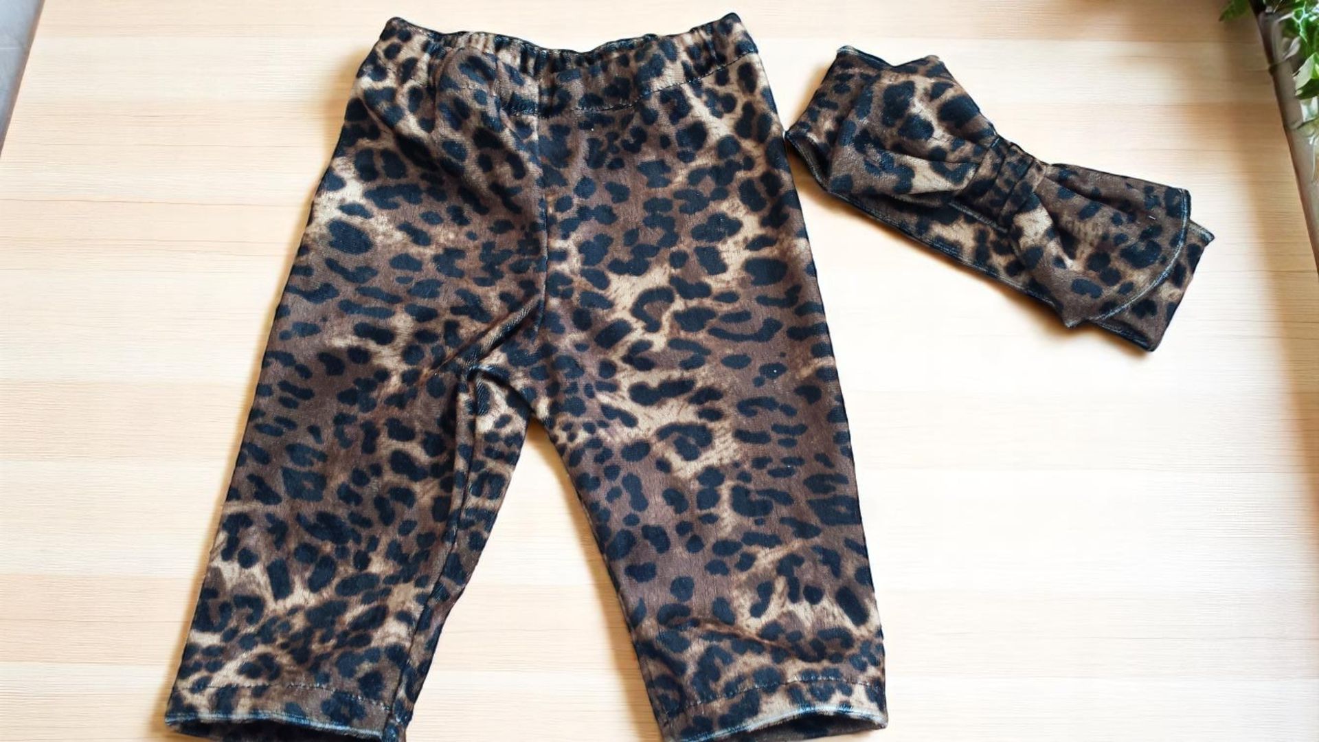 Leopard-print toddler leggings and a matching headband set laid flat on a light-colored wooden surface.