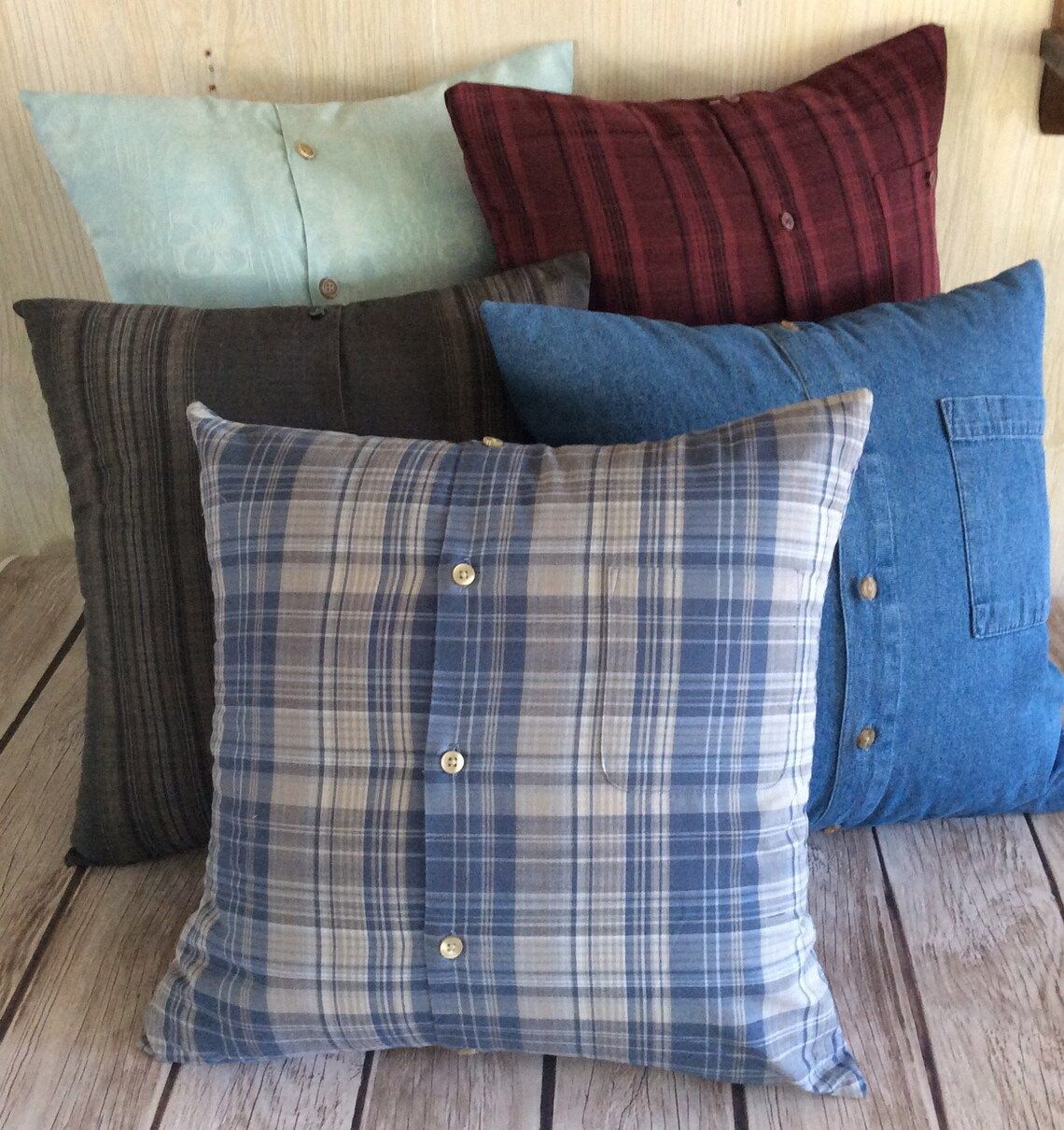 Five decorative pillows made from upcycled men’s dress shirts, arranged against a wood-paneled wall.