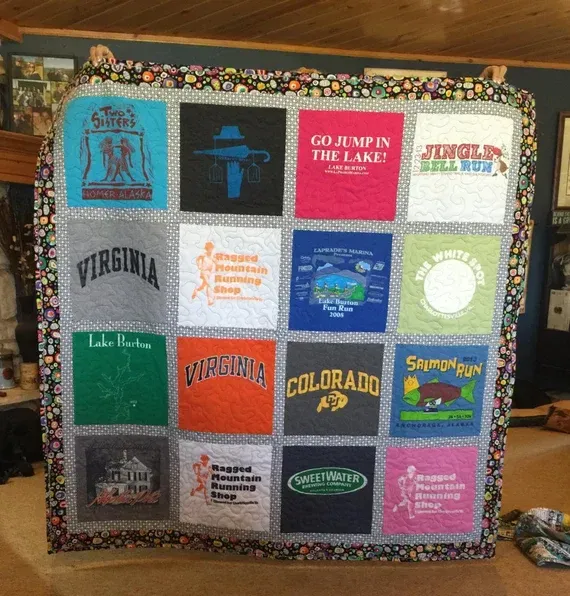 A handmade quilt made from sixteen colorful t-shirt squares with various logos and text, bordered by a patterned fabric.