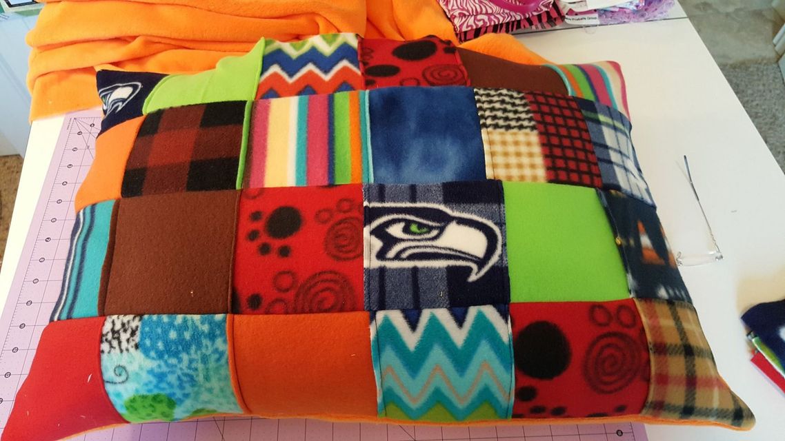 A patchwork pillow made of colorful fabric squares in various patterns, including a Seattle Seahawks logo.