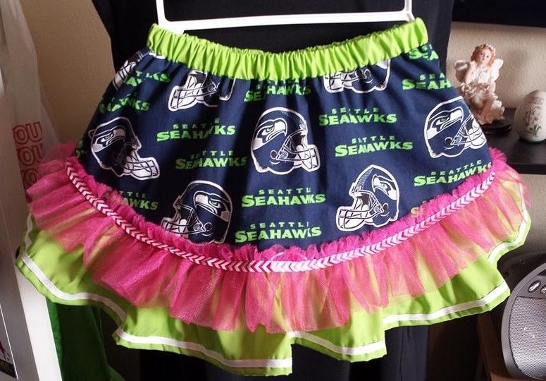 A Seahawks-themed skirt with navy blue fabric, lime green trim, and a bright pink tulle ruffle overlay on a white hanger.