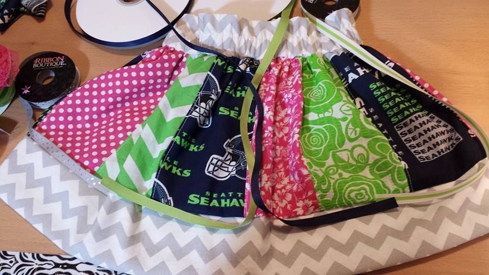 A patchwork skirt made of Seattle Seahawks, chevron, floral, and polka-dot fabrics, lying on a wooden surface with ribbon.