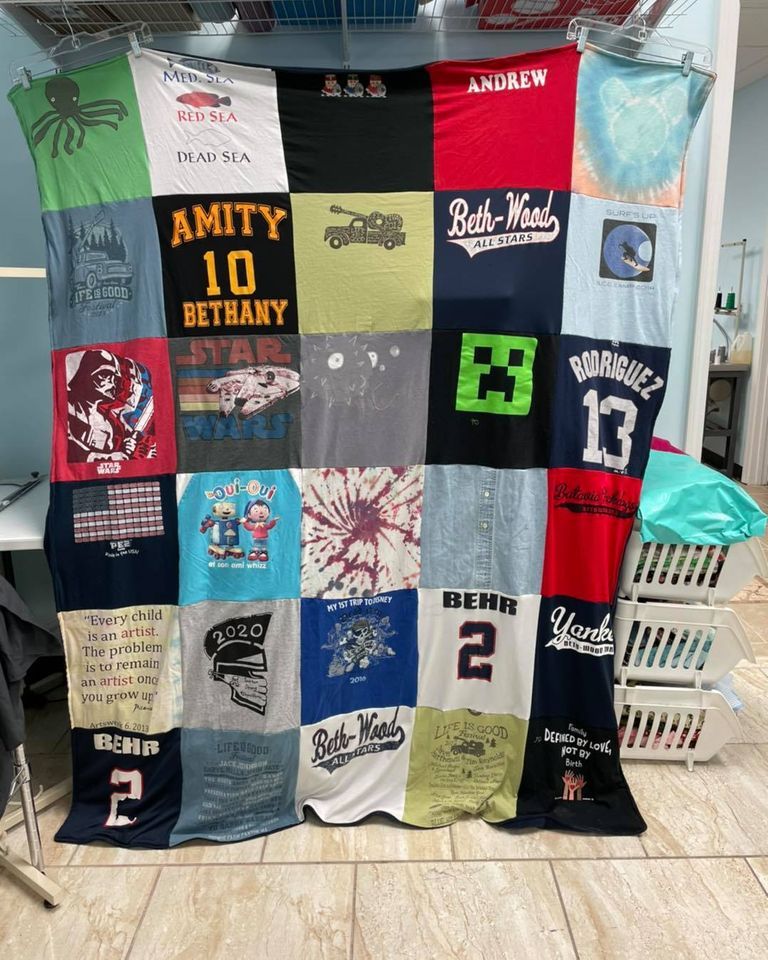 A colorful t-shirt quilt featuring assorted graphics, logos, and text squares arranged in a five-by-five grid.