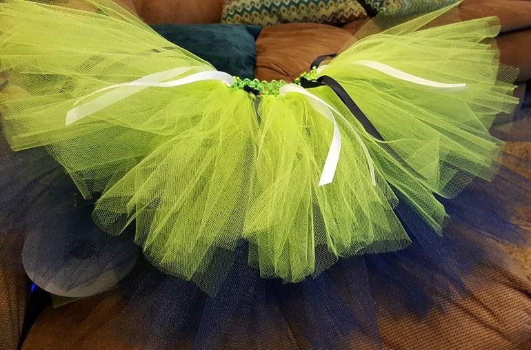 A layered lime green tutu with white and black ribbon accents, resting on a brown textured surface.