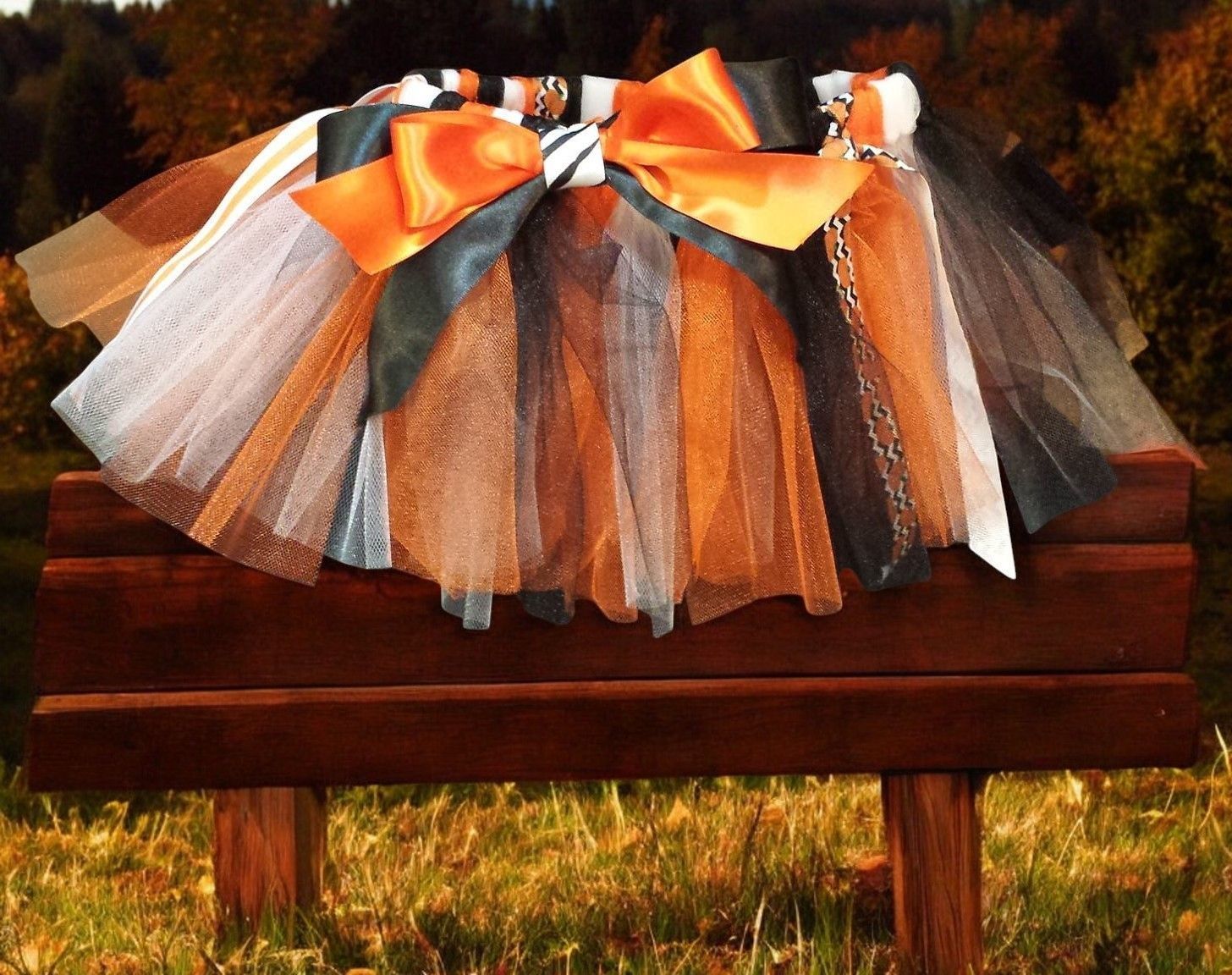 A tutu featuring layers of black, orange, and white tulle, accented with a large orange satin bow, resting on a bench.