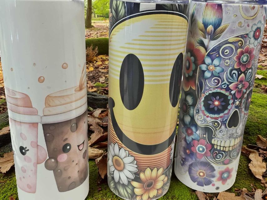 Three tumblers with different designs: cute bubble teas, a retro smiley face with flowers, and a colorful floral sugar skull.