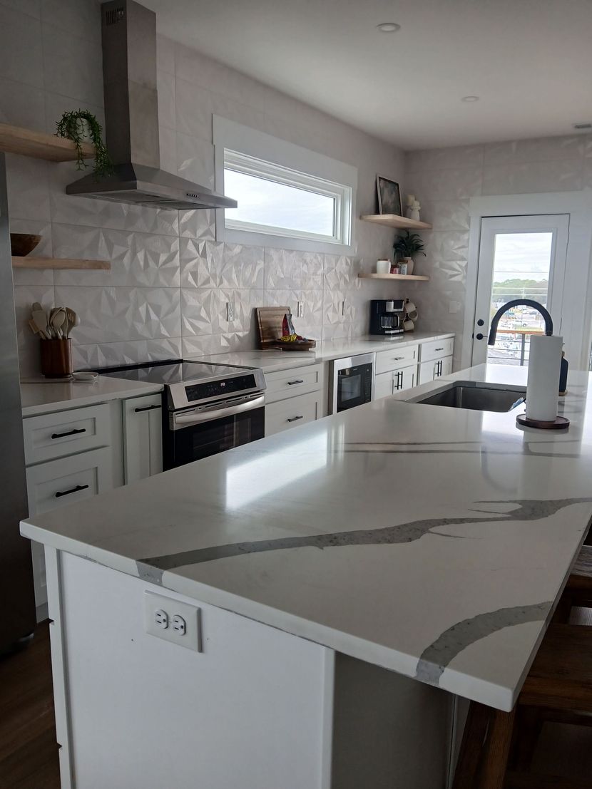 Bright modern white kitchen with large island, gray countertops, oven, and windowed door.