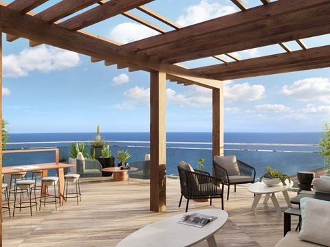 Wooden pergola over a deck with seating, overlooking the ocean on a sunny day.