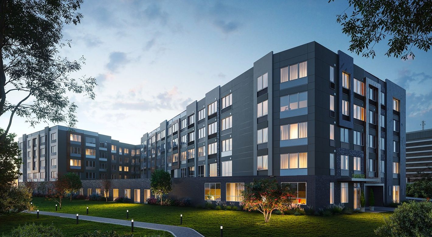 Modern multi-story apartment building with lighted windows in a dusk setting.