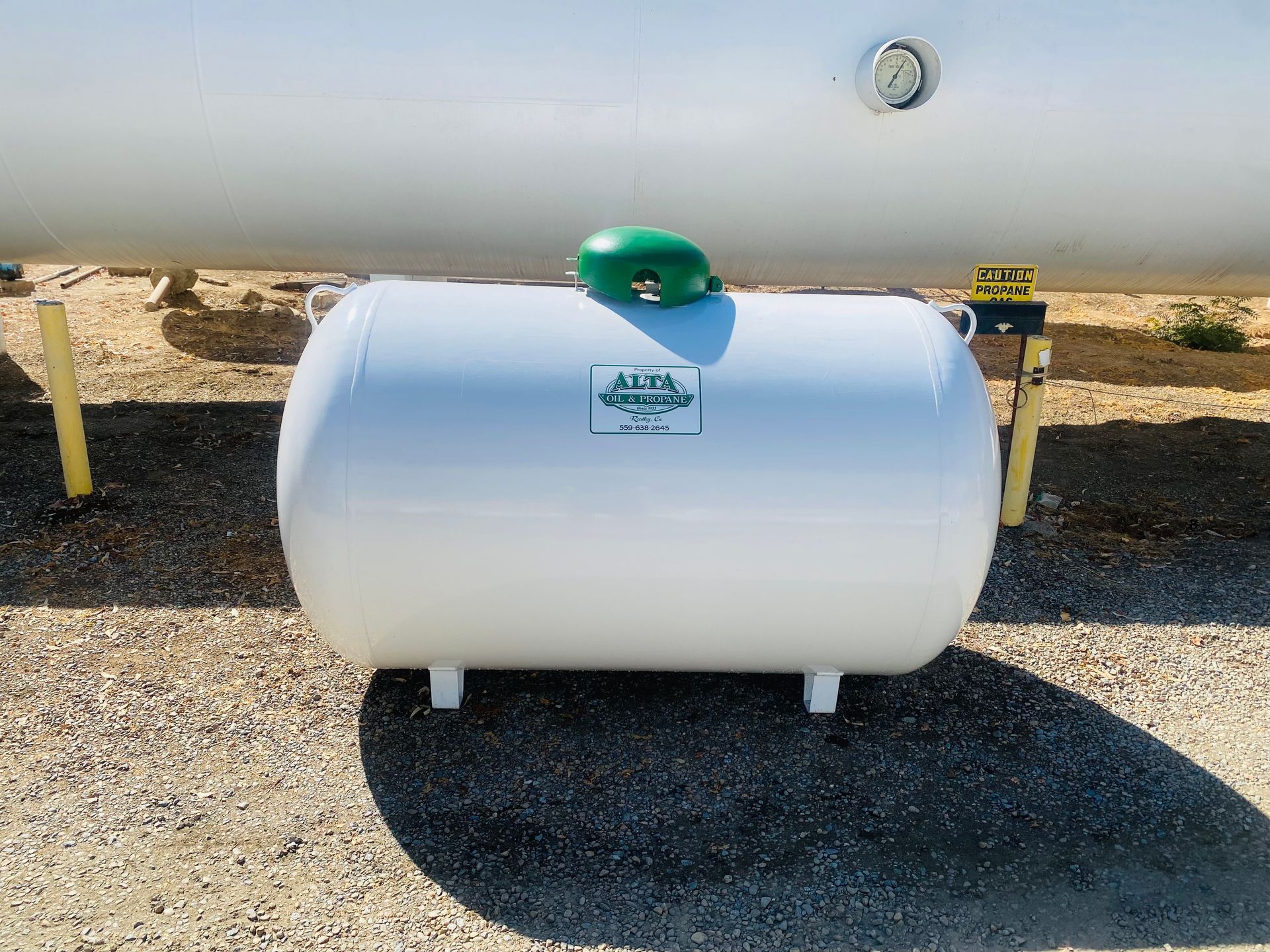 White propane tank with green cap, outdoors.