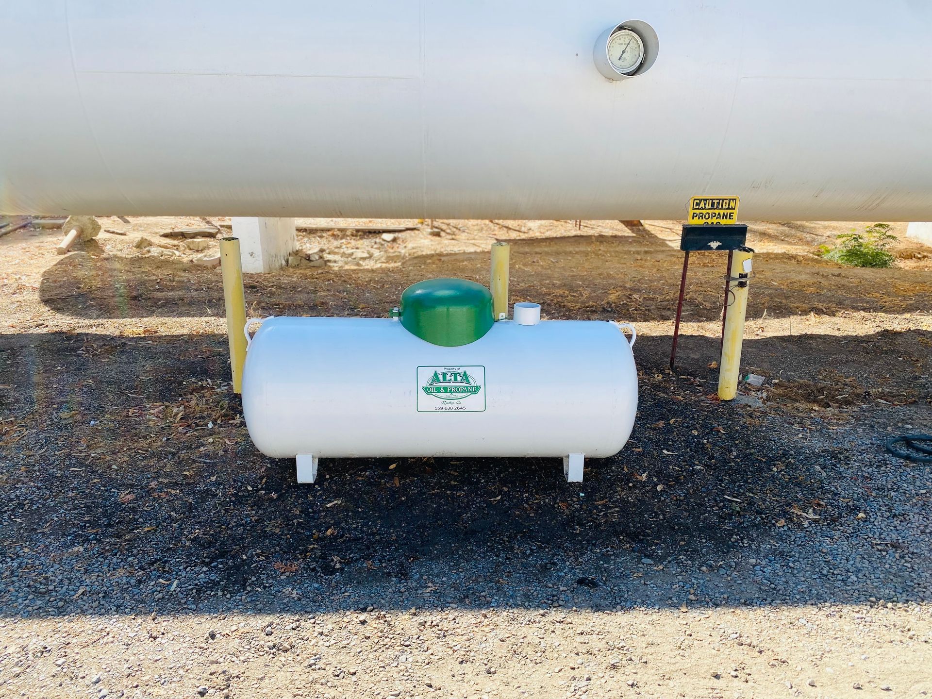 White propane tank under larger tank, with green cap and gauge. Ground setting.