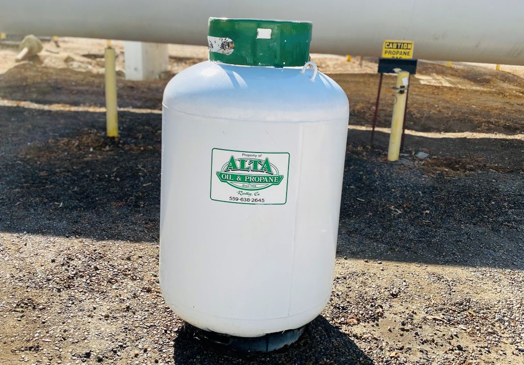 White propane tank with a green top and label, outdoors.