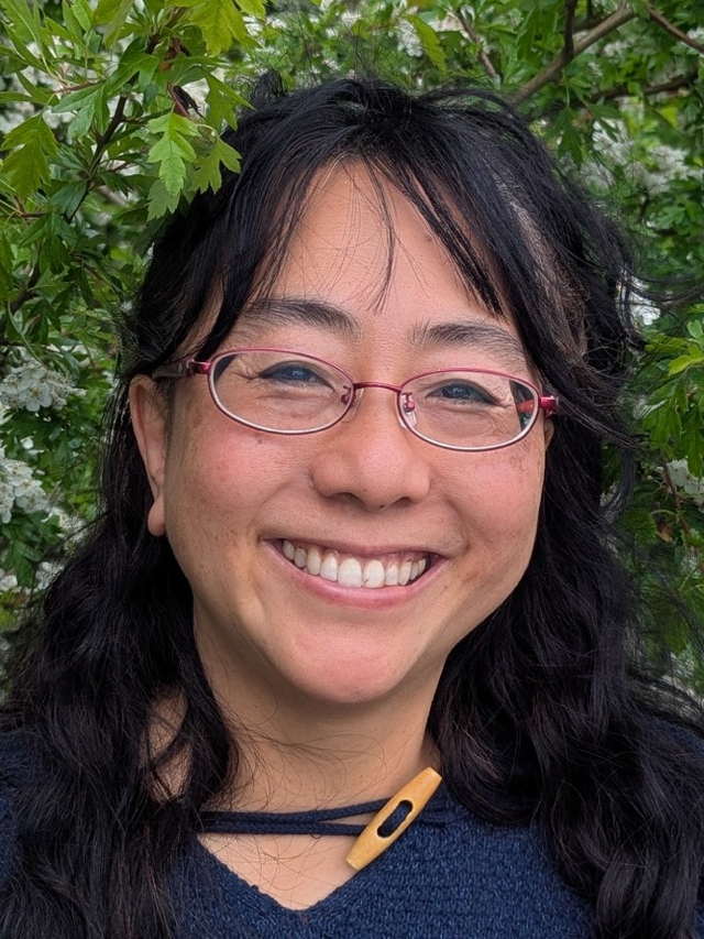 Dr Urara Donohoe smiling in front of a flowering hawthorn hedge