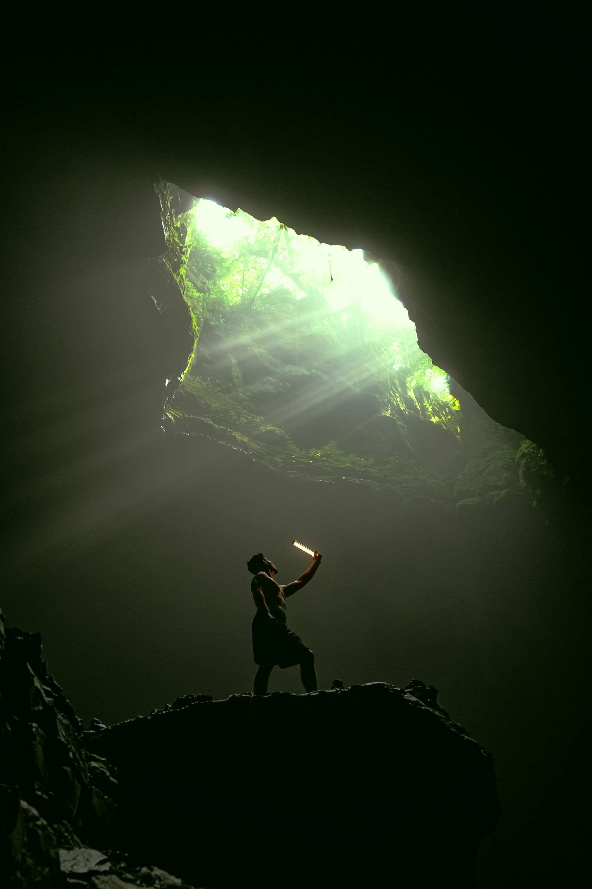 Silhouette of a person standing in a dark cave, reaching toward bright green light from above.