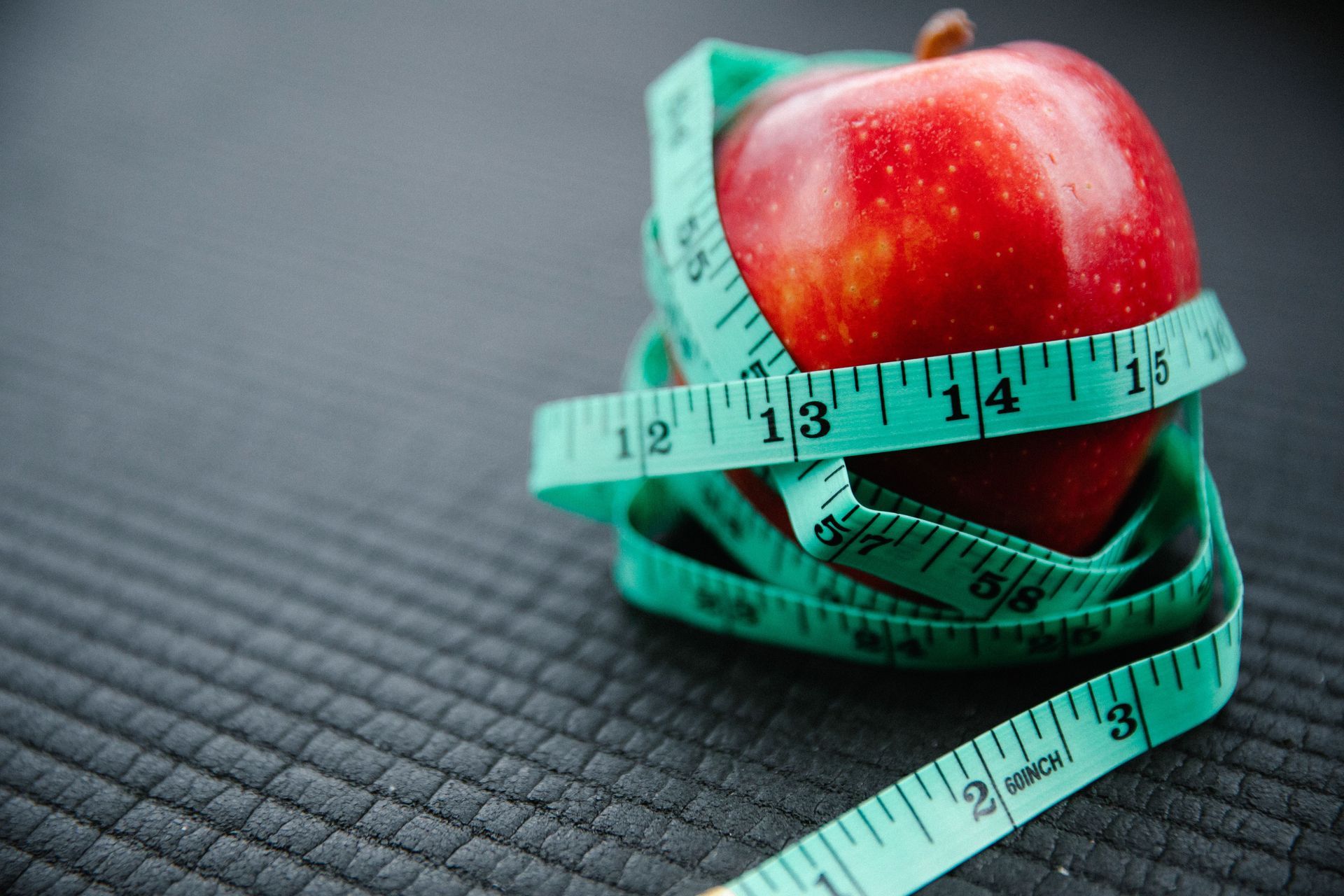 Red apple wrapped with a teal measuring tape on a dark textured surface