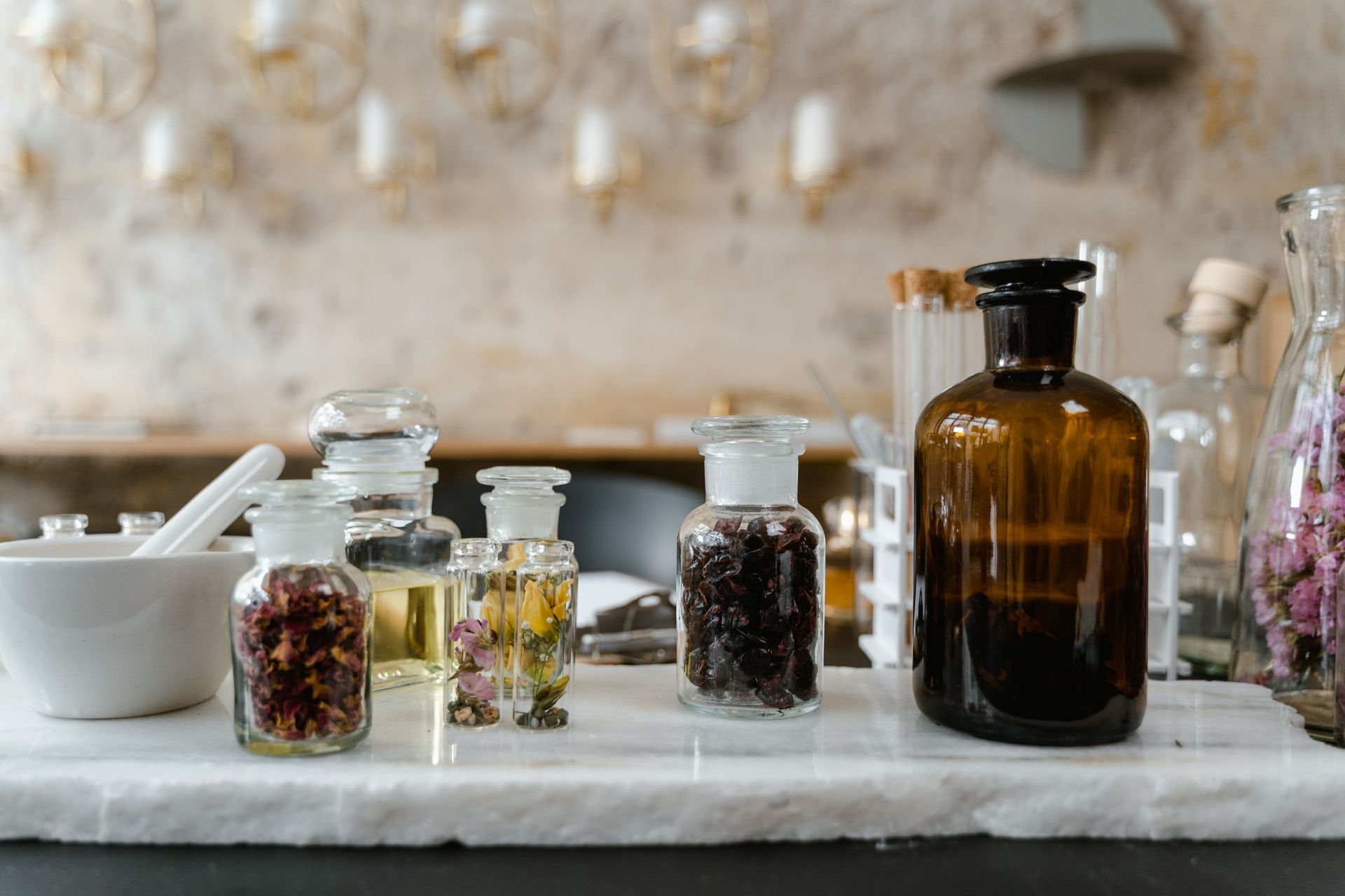 Assorted glass jars and bottles with herbs and liquids on a marble counter in a rustic kitchen