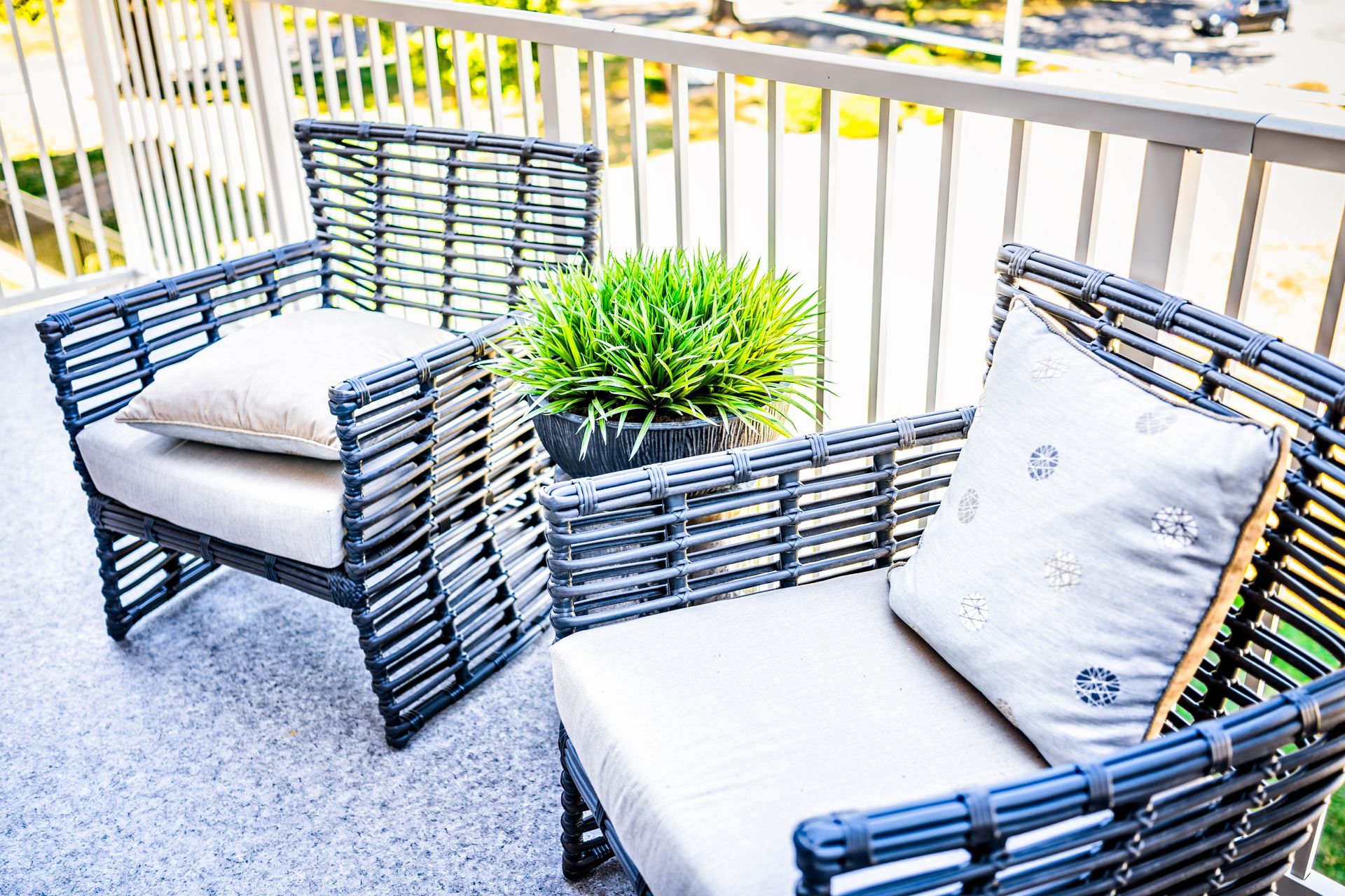 A balcony with two wicker chairs and a potted plant.