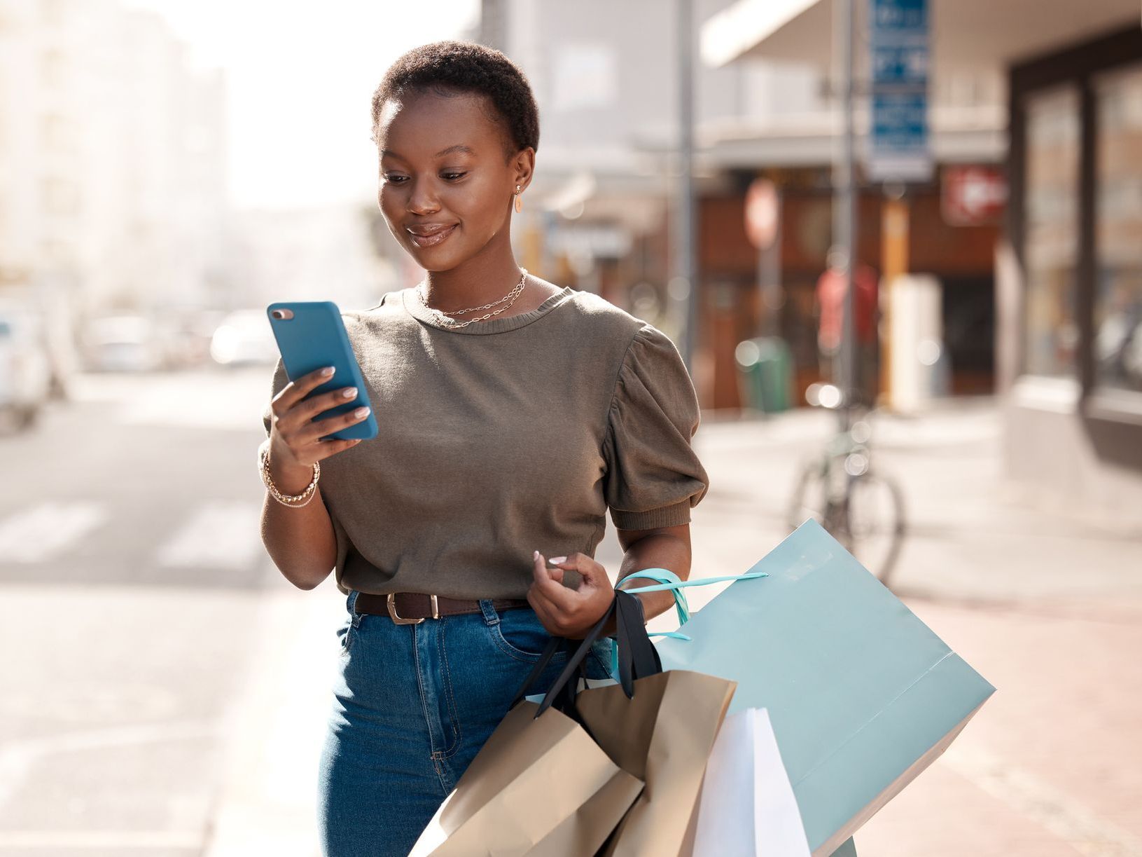 A woman is walking down the street with shopping bags and looking at her phone.