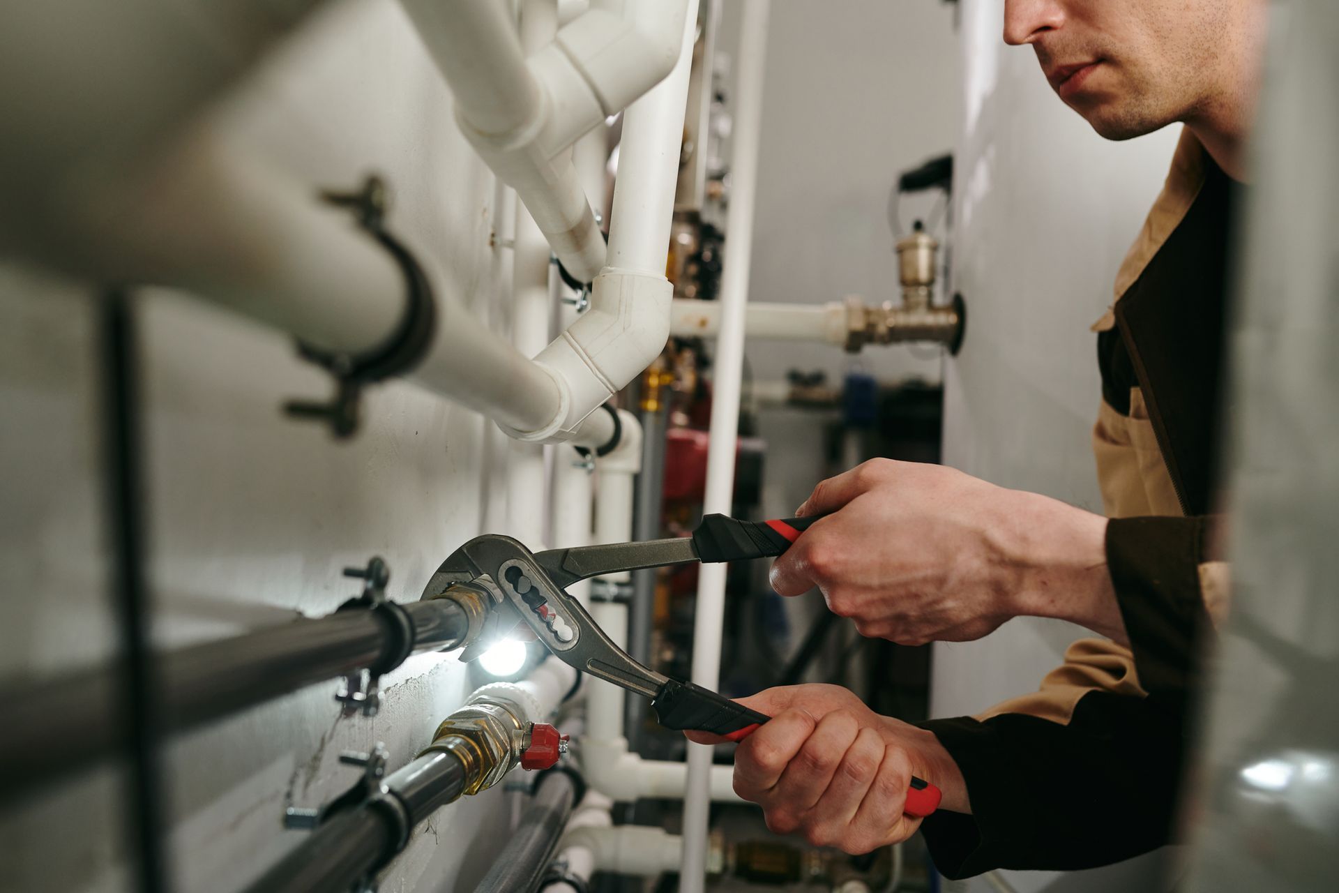 Plumber using pliers to tighten a pipe connection in a utility room.