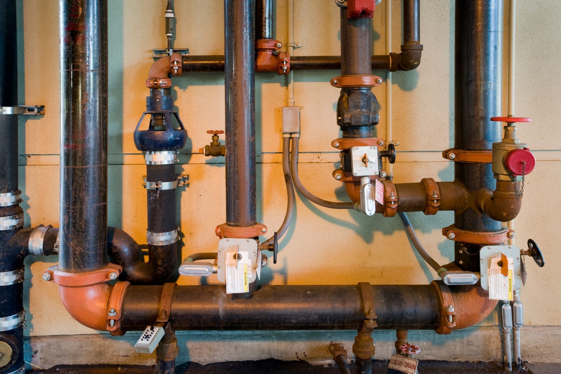 Black and orange pipes with valves against a beige wall; an industrial setting.