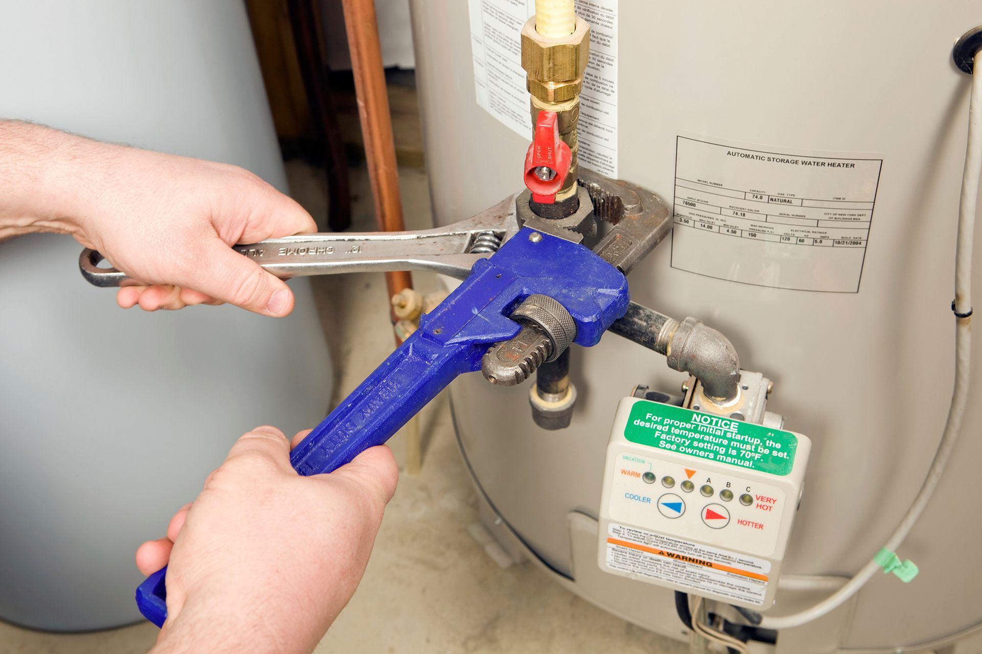 Person using a wrench to tighten a pipe connection on a water heater in a utility room.