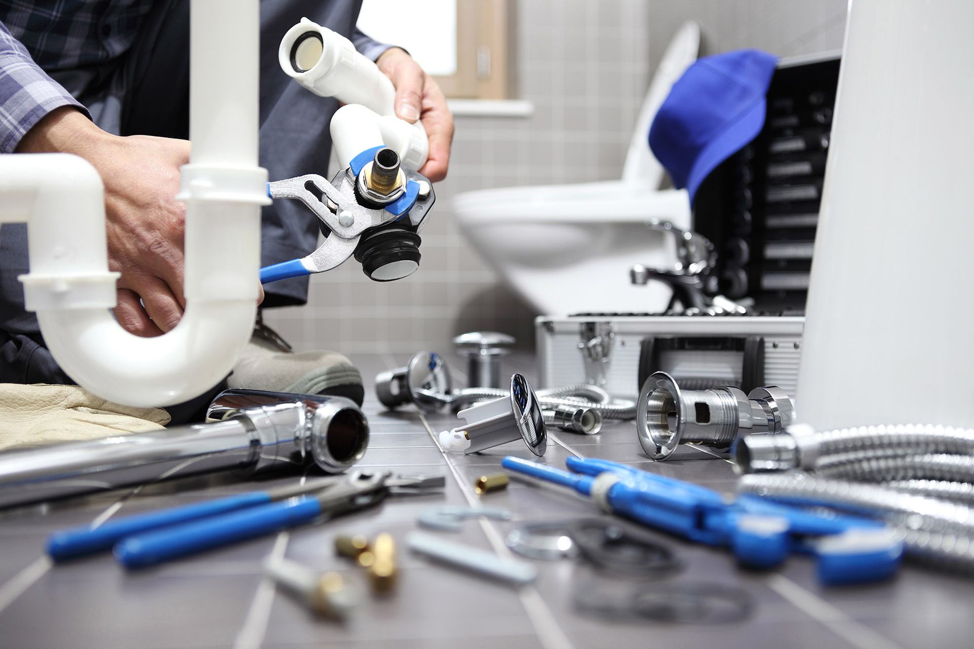 Plumber working on pipes and tools in a bathroom, with a toilet in the background.