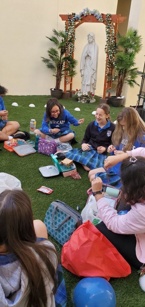 People sitting in a circle on a grassy floor near a decorated shrine, sharing food and conversation.