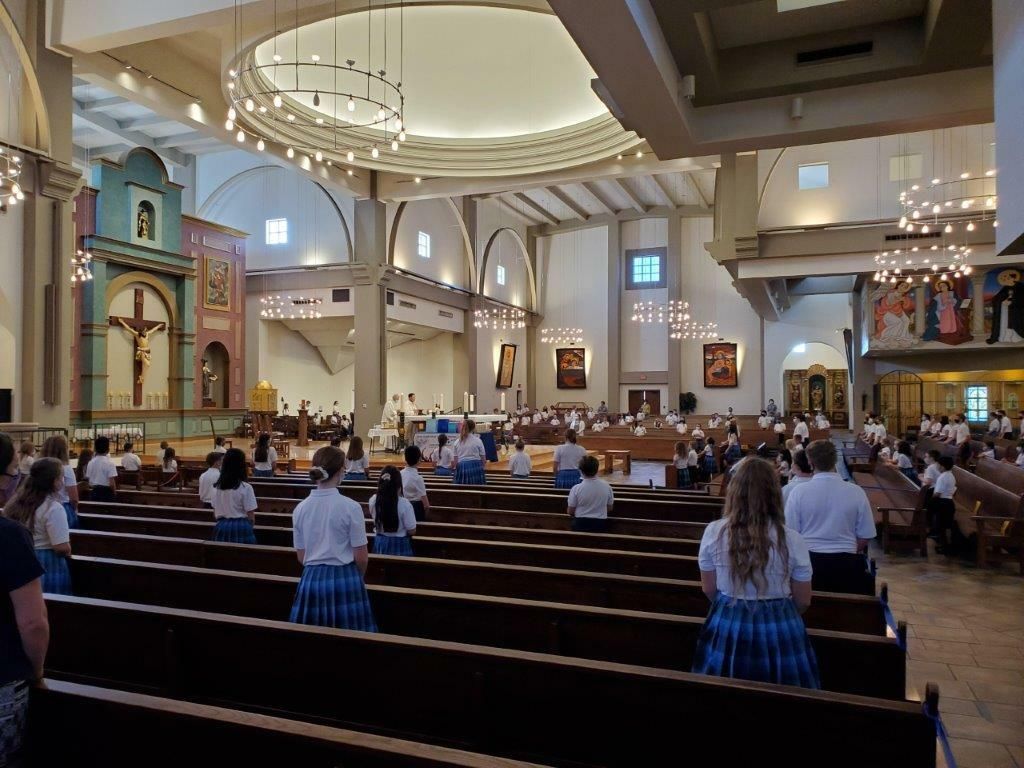 Church interior with people seated in pews during a service, with a large altar and arched ceiling