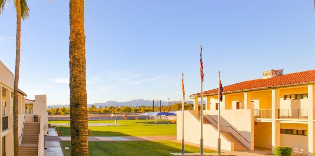 Sunny campus courtyard with beige buildings, palm trees, and distant mountains under a clear blue sky