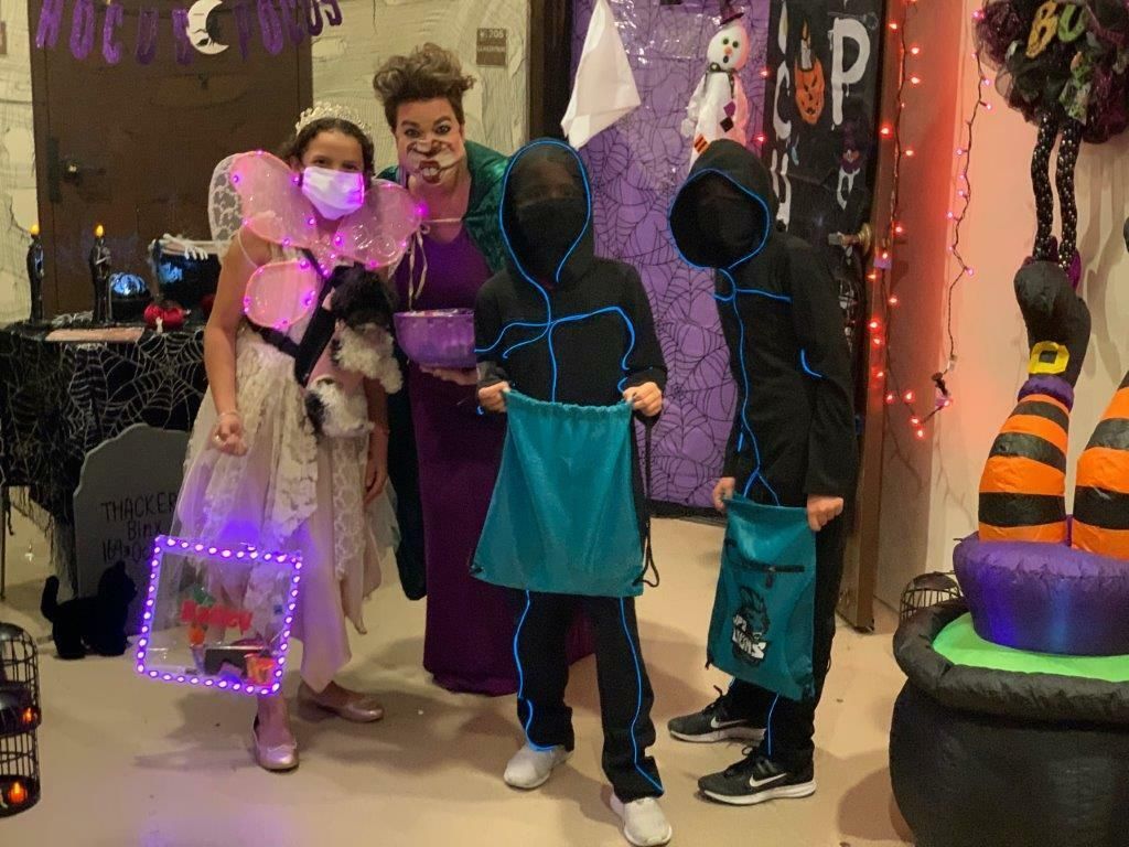 Three costumed trick-or-treaters posing indoors with glowing Halloween props and bags