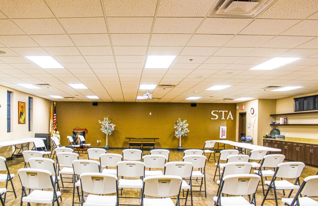 Empty community room with rows of folding chairs facing a stage and wooden podium.