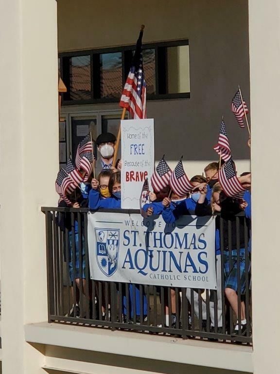People on a balcony holding American flags and a St. Thomas Aquinas banner