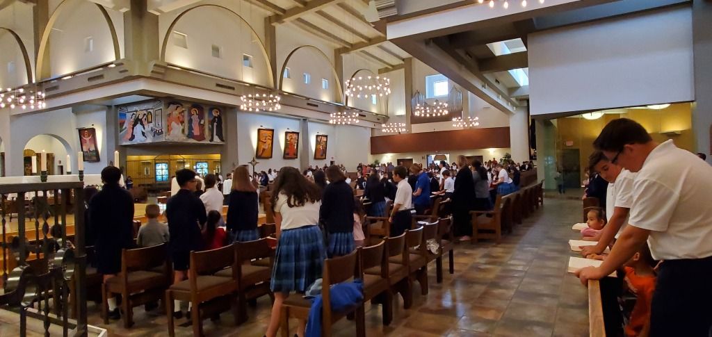 Busy church interior with people seated in pews and a man leaning at the right side aisle
