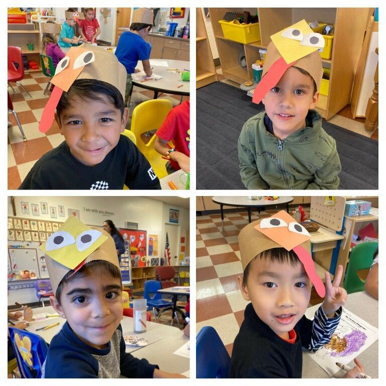 Four children smiling in a classroom, each wearing a handmade paper turkey hat.