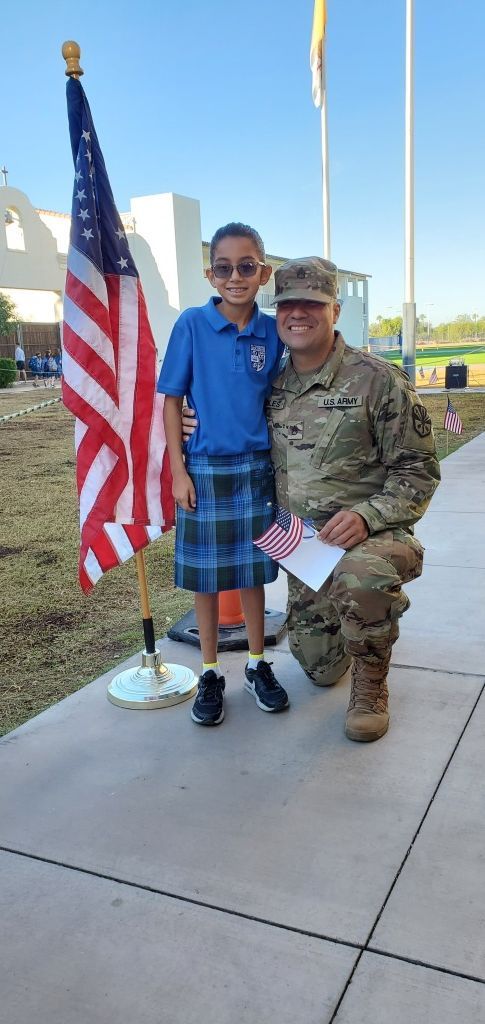 Child and soldier posing with an American flag outdoors at sunset
