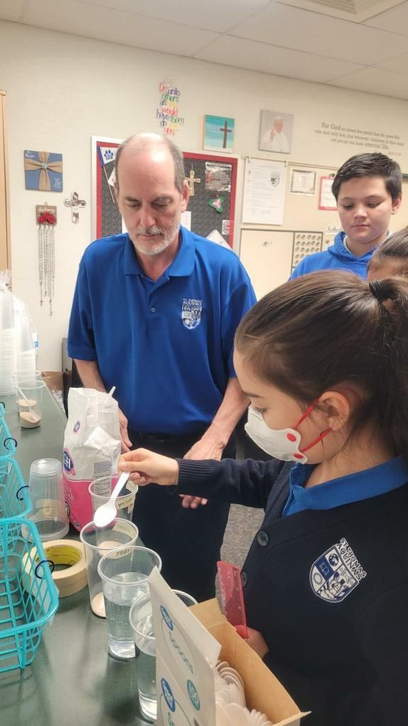 Students and teacher observe a science experiment with glassware in a classroom