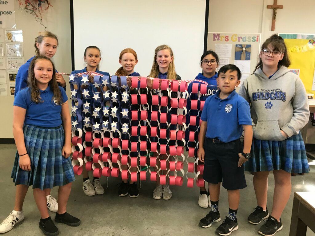 Students holding a large U.S. flag made of red, white, and blue plastic cups in a classroom
