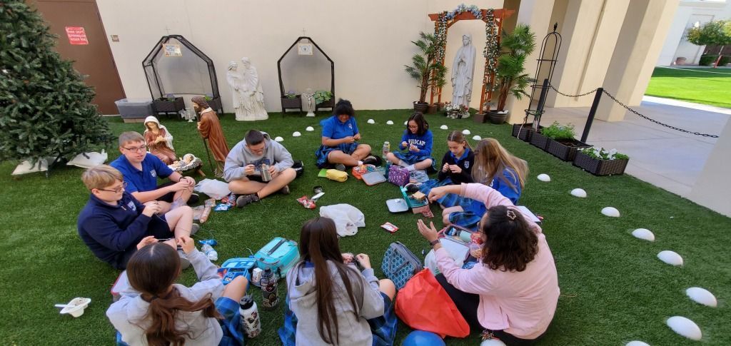 People seated in a circle on artificial grass in a courtyard, listening and chatting during an outdoor activity