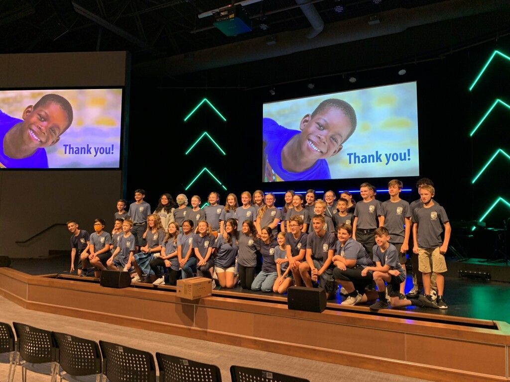 Group photo onstage with people posing in front of screens showing “Thank you!” and a smiling face