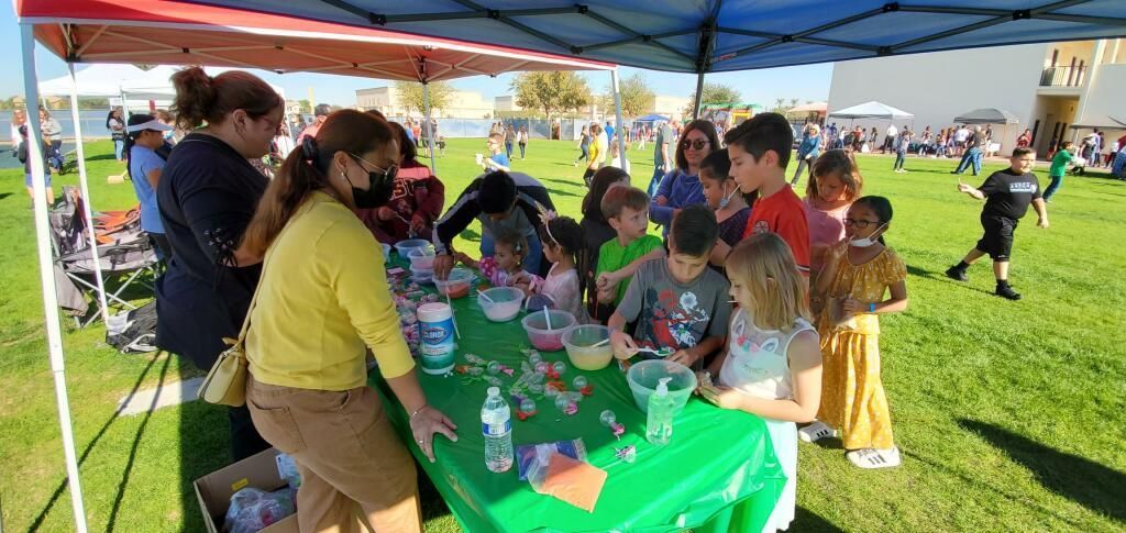 People gathered around a green craft table under a canopy at an outdoor event.
