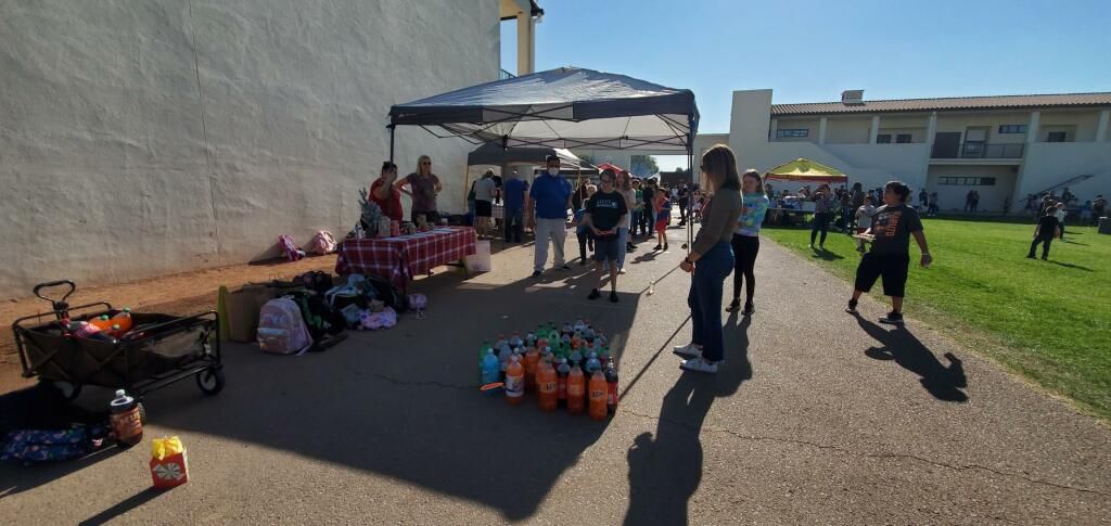 People gathered outdoors beside tables of flowers and orange items on a sunny day