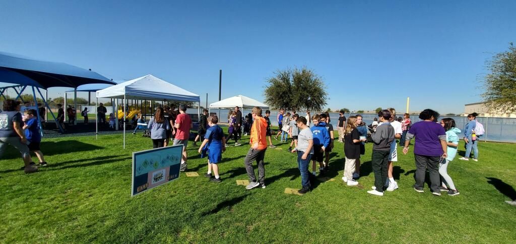 People walking on a grassy field at an outdoor community event under a blue sky.