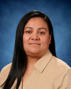 Studio portrait of a person with long dark hair in a beige shirt against a blue background
