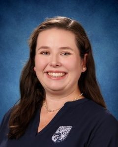 Smiling person in a navy shirt against a blue studio backdrop.