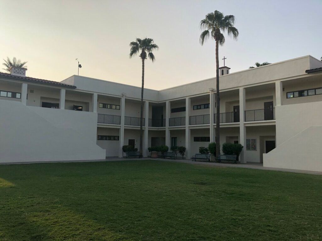 Courtyard of a white two-story building with palm trees and a green lawn at sunset